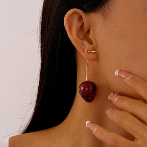 Close-up of model wearing elegant long red cherry-shaped acrylic earrings with gold bars