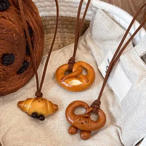 Dettaglio dei ciondoli a forma di croissant e pretzel con sorrisi su cordino marrone