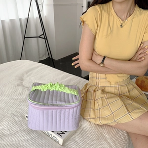 Detailed shot of purple quilted makeup bag with green handle on a white textured background