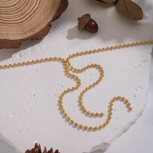 Detail of golden ball chain necklace on rustic wood and white textured background