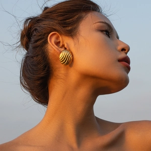 Gros plan de boucles d'oreilles ovales dorées à texture ondulée sur un modèle au coucher du soleil