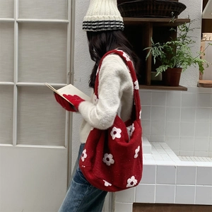 Detail view of red plush tote bag with white floral pattern on shoulder of model