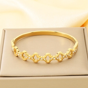 Detailed view of luxury gold stainless steel hollow bangle with cubic zirconia on beige stand