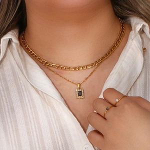 Detail of layered gold necklaces with black pendant and minimalist zircon rings on model