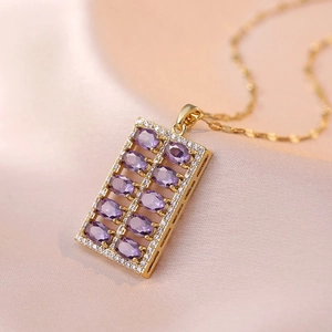Detailed close-up of a golden rectangular pendant with purple and clear zircon stones