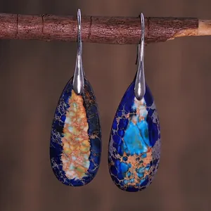 Detail view of teardrop natural emperor stone earrings on a rustic wood branch