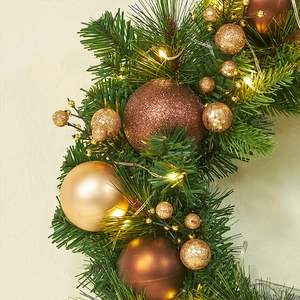 Christmas wreath with warm LED lights, gold ornaments and pine needles on beige background