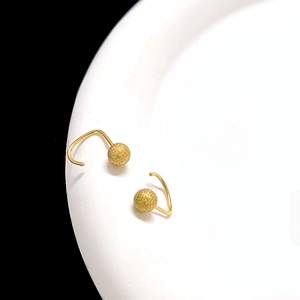 Macro shot of minimalist matte gold spherical earrings on a clean white ceramic tray