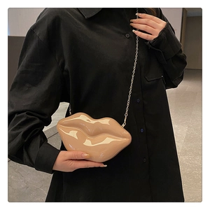 Detail view of a beige lip-shaped clutch with gold chain on black shirt background