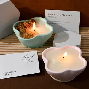 Macro shot of lit petal-shaped scented candles with dried flowers in ceramic bowls