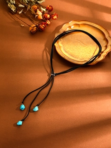 Detail of bohemian turquoise stone pendant with black rope chain on vintage tray