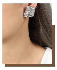 Detailed view of silver square stud earrings with unique vertical woven texture on model
