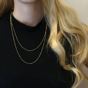 Detail of layered gold snake chain necklace with small beads on a black turtleneck