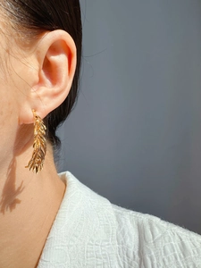 Detail of golden feather tassel earring on ear showing fine metal texture and shiny finish