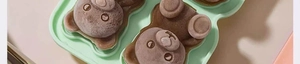 Close-up of four frozen brown bear-shaped ice cubes inside a light green silicone mold