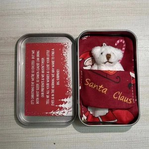 Detailed view of a white plush bear in a silver metal box with a Santa Claus themed quilt