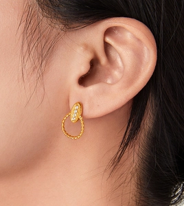Detail of twisted gold earrings with rhinestone oval pendants on a model's ear