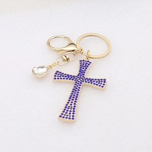 Detail of golden keychain featuring blue rhinestone cross and teardrop zircon pendant
