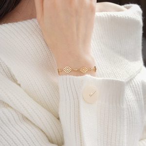 Close-up of gold hollow diamond-shaped knot bracelet on a model wearing white knitwear