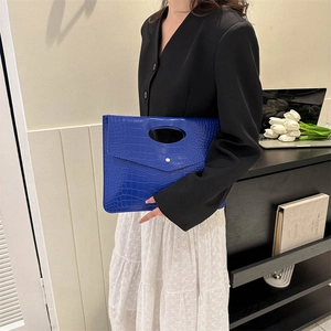 Blue crocodile pattern leather clutch bag held by model in modern fashion setting