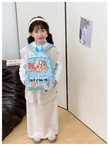 Toddler wearing a light blue cartoon backpack with capybara print in a cozy home setting