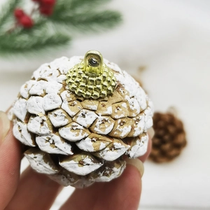 Macro shot of natural pine cone with white snow effect and golden hanging metal loop