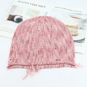 Close-up of pink knitted beanie with edgy distressed hole design and fringe details
