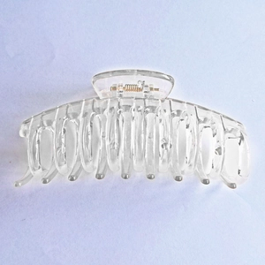 Close-up of a large transparent hair claw clip with a strong metal spring and curved teeth