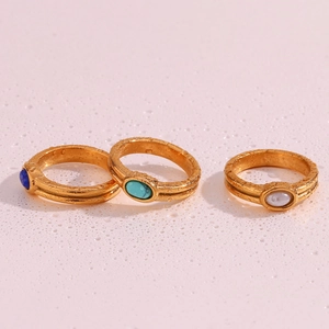 Three gold rings with colorful natural stones on a pink textured water drop surface