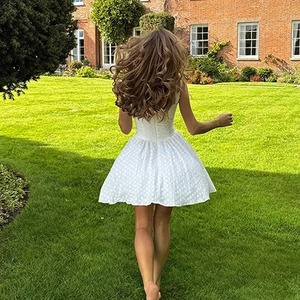 Back view of a white textured backless A-line mini dress worn by a woman running on a lawn