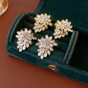 Detailed macro view of silver and gold crystal floral earrings in a green velvet box