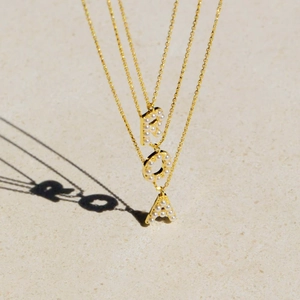 Three gold-plated necklaces with pearl-inlaid letters R, O, and A on a stone surface