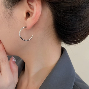 Close-up of minimalist silver-toned geometric C-shaped earrings worn by a model