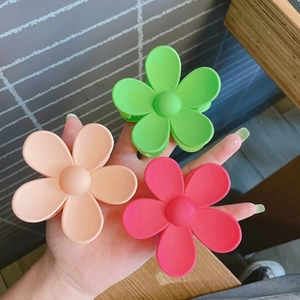 Three large matte floral hair claws in pink, green, and rose red held for size display