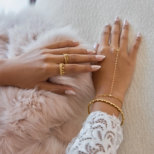 Detailed close-up of 18K gold crown rings with rhinestones on a lace-sleeved hand