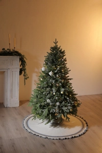 Close-up of Fair Isle knit Christmas tree skirt with tassels under a snowy decorated tree