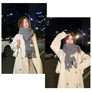 Detail of grey fringe scarf with GE label worn by model in a night street setting
