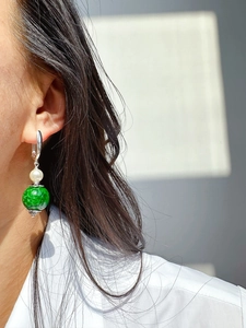 Detail of silver drop earring featuring a white pearl and round green gemstone on model