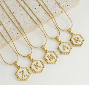 Detailed macro view of 18k gold snake chains with hexagonal shell initial pendants