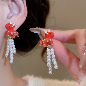 Close-up of red enamel horse stud earrings with pearl tassels on a female model