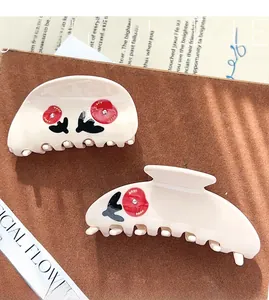Detail of cream rose hair claw set with red floral patterns and crystal accents