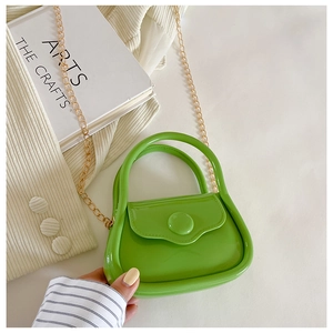 Close-up of a mini bright green jelly bag with gold chain strap on a woven fabric base