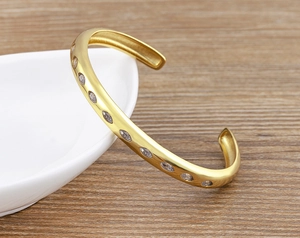 Detail of 18k gold plated cuff bracelet with oval white zircon stones on ceramic plate
