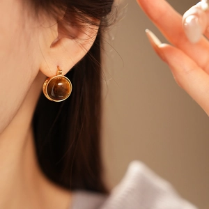 Gros plan d'une boucle d'oreille en plaqué or et pierre œil de tigre sur un mannequin