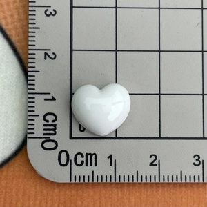 Close-up of white resin heart charm measured at 1.2cm x 1cm with ruler reference