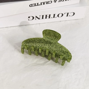 Detail of green glitter claw clip with shark fin design on a neutral minimalist background