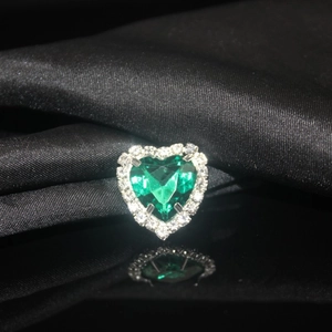 Macro detail of a heart-shaped emerald green crystal with white rhinestone halo on black silk