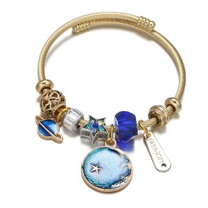 Detail of golden spiral bangle featuring blue planet charms and diamond star beads