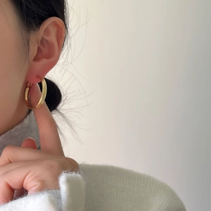 Detailed close-up of a minimalist brushed gold hoop earring worn on a female ear