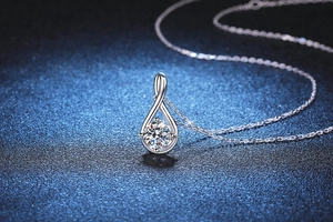 Detailed close-up of water drop moissanite pendant on silver chain against blue backdrop